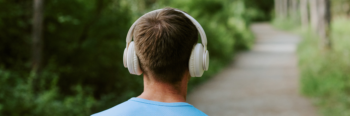 Back of a mans head wearing headphones and a blue T-shirt walking outdoors on a path